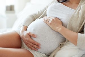 Kobieta w zaawansowanej ciąży z czułością obejmuje swój brzuch