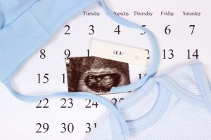 Test ciążowy z pozytywnym wynikiem, USG dziecka i niebieskie ubranka dla noworodka na kalendarzu, koncepcja powiększenia rodziny i oczekiwania na dziecko